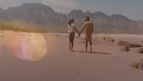 multiple light spots floating against african american couple holding hands walking at the beach