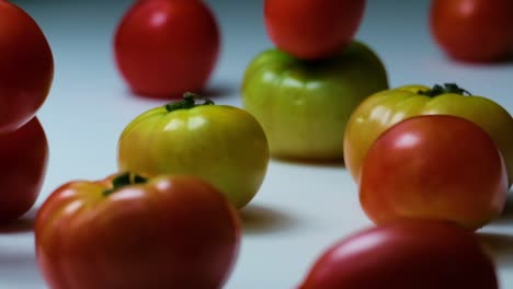 Slow-Motion-Shot-of-Big-Tomatoes-Falling-on-Other-Tomatoes-Laying-on-a-White-Surface