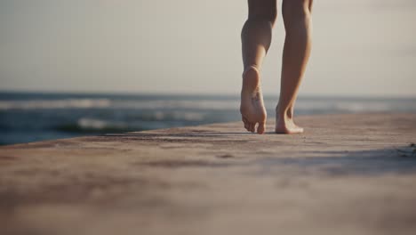 Woman-feet-walking-on-concrete-path-on-shore-of-Bali-during-golden-sunlight