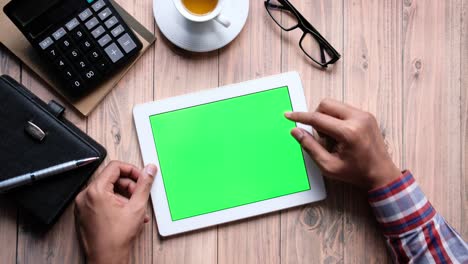 persona usando una tableta con una pantalla verde en un escritorio de madera