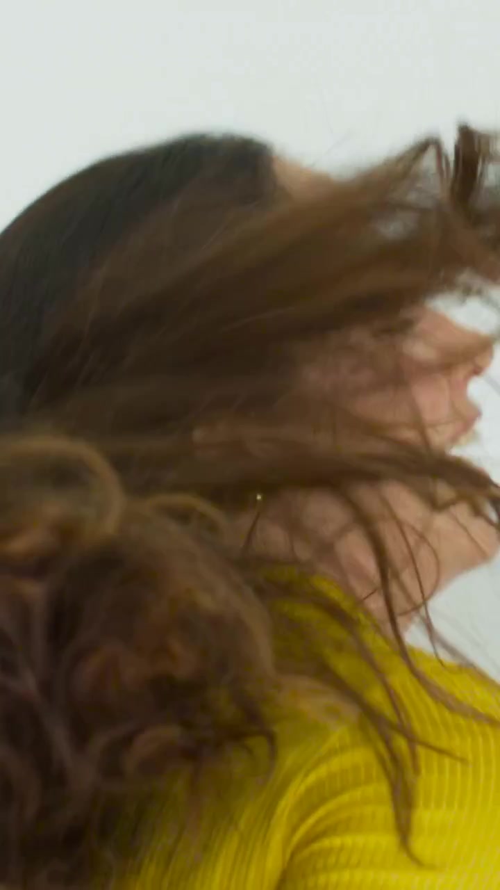 Video verticale: Donna che inclina la testa facendo ondeggiare i capelli in studio, dolcevita giallo per ritratto.
