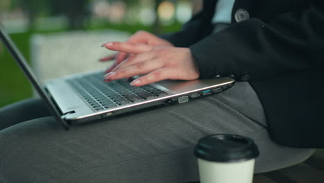 Close up of woman with polished nails typing on laptop in outdoor setting with greenery, blurred trees, and soft bokeh light creating calm work atmosphere ideal for remote or freelance productivity