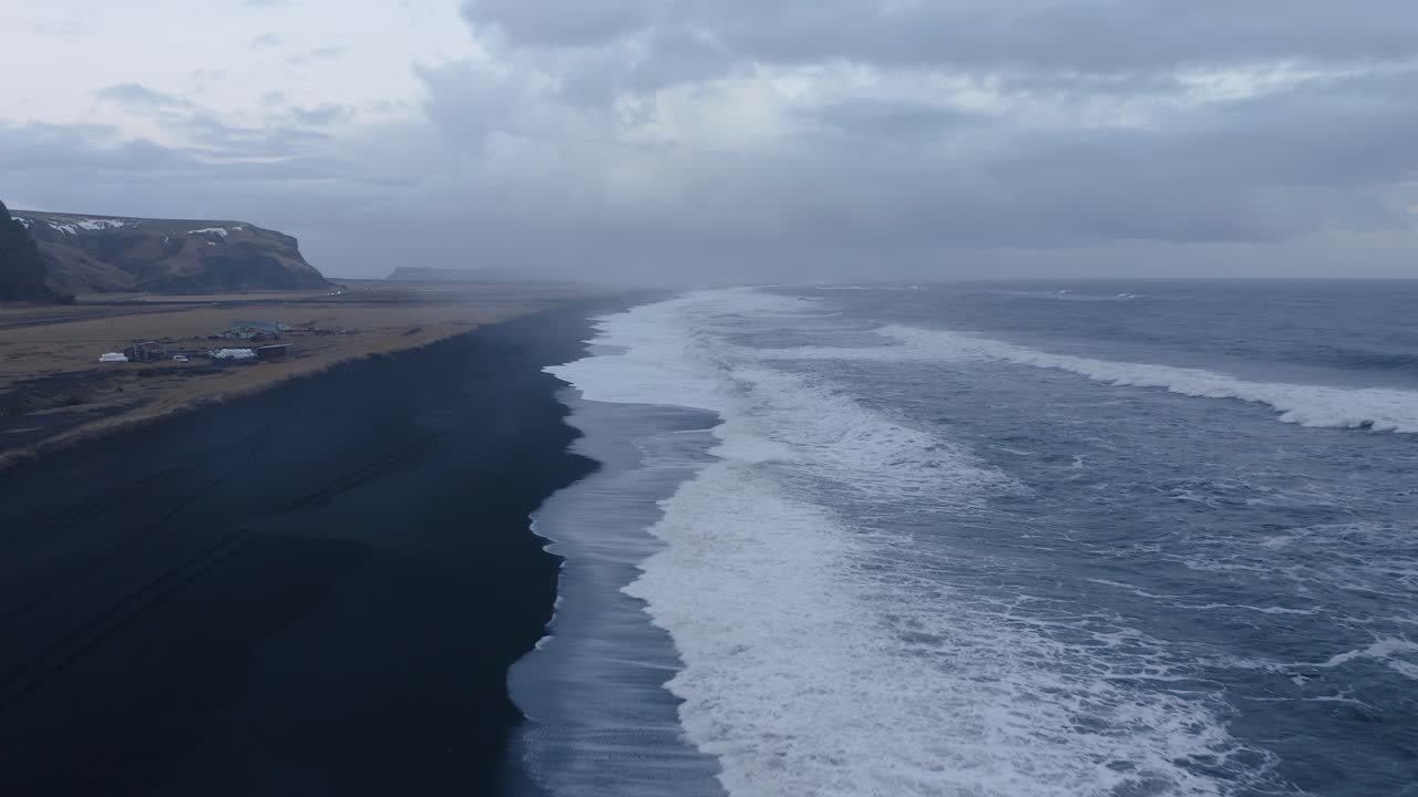 volando hacia un tramo de playa de arena negra con olas tormentosas en víkurfjara cerca de vik en islandia