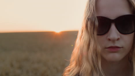 retrato de una adolescente con gafas de sol en el fondo de un campo de trigo donde se pone el sol