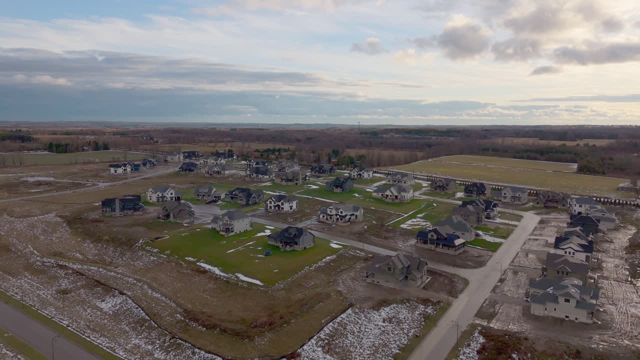 Drone view over Alton, Caledon subdivision with partly built houses, vacant lots and patchy snow on open fields under a cloudy sky, showing Ontario expansion