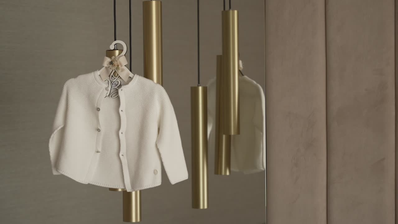 Soft white baby cardigan on a personalized hanger, elegantly displayed with golden accents