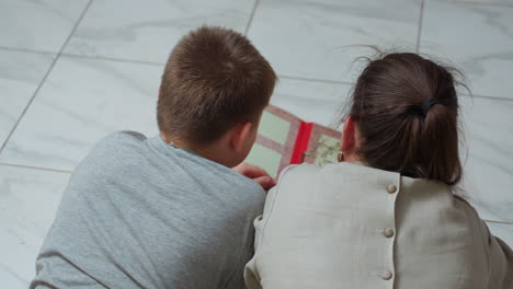 back view woman and boy lying on white marble floor closely reading open book quiet cozy atmosphere relaxing bonding moment indoors family togetherness casual clothing warm peaceful environment