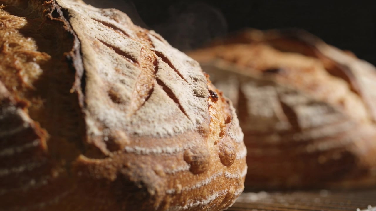 Showing artisan sourdough loaf cooling after oven on wood board, with banneton coils and steaming