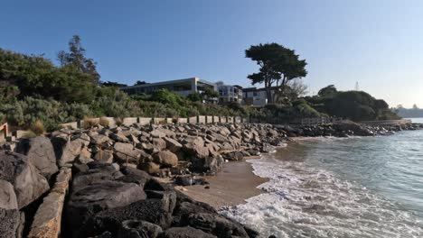 waves crashing on rocky shore near luxury houses