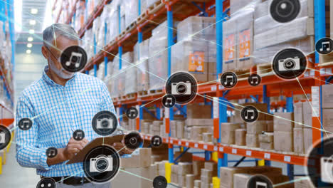 Animation-of-network-of-connections-with-icons-over-caucasian-male-worker-working-in-warehouse