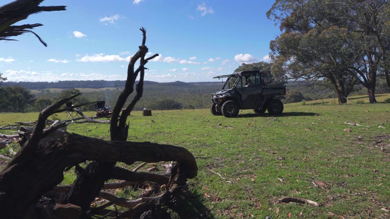 Filmisk rörlig gimbal-tagning som avslöjar ett robust jordbruksfordon bredvid en avlägsen lägereldplats med utsikt över vidsträckt australisk buskmark under en klarblå himmel