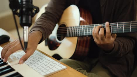 close up hand professional songwriter playing guitar with tablet and audio equipment for mixing and mastering music. male composing a song with piano keyboard at recording studio. musician concept