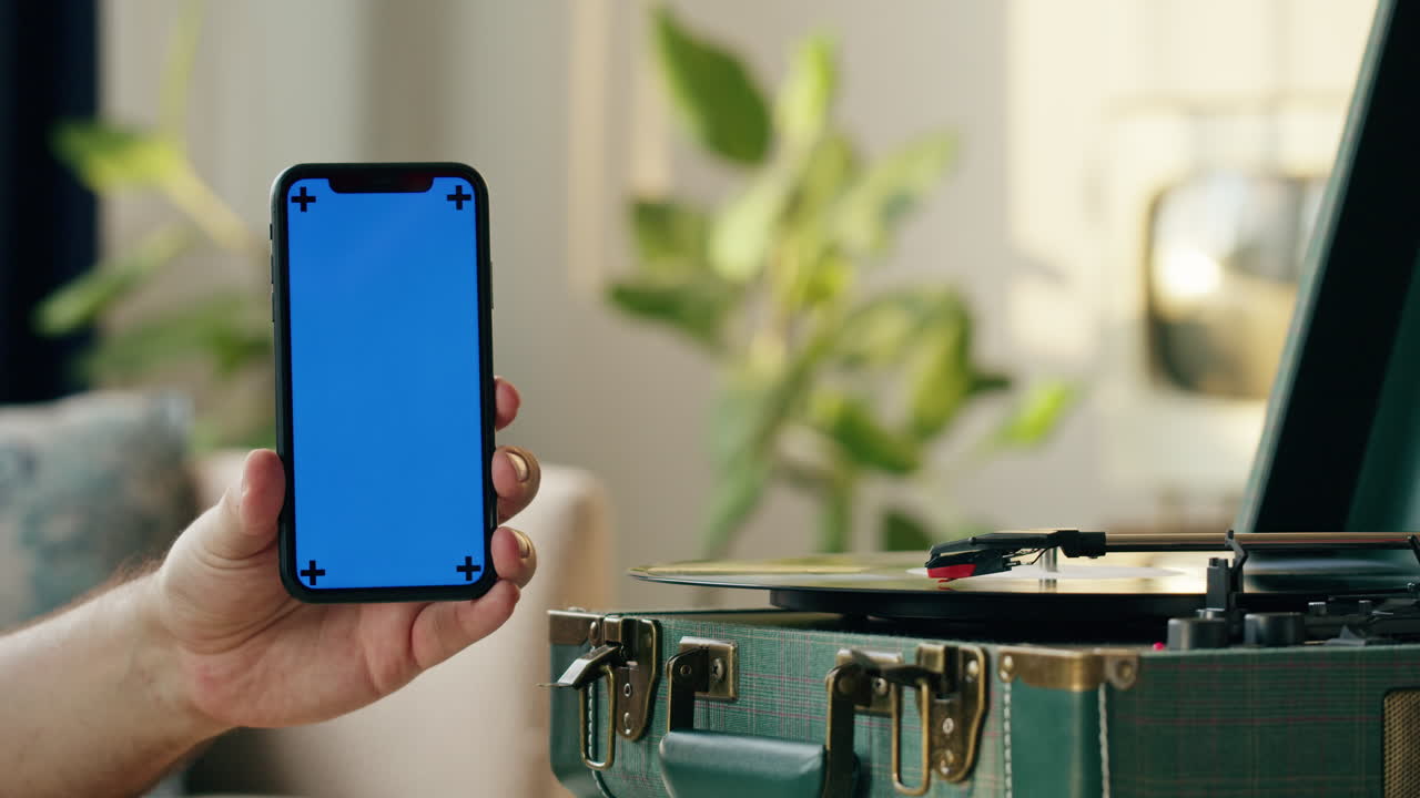 Mano che tiene uno smartphone con schermo blu accanto a un giradischi vintage