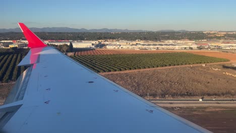 left wing view of a medium size jet during the landing with a warm afternoon light and the jet’s shadow over the ground