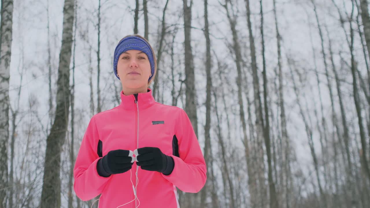 The girl before the morning winter jog inserts headphones in the ears and is preparing to run through the natural Park in slow motion. Listening to music while running. Learn foreign languages