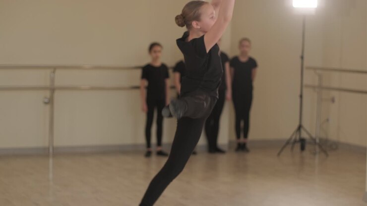 un grupo de jóvenes estudiantes de ballet con ropa de baile negra practicando posiciones en un amplio estudio de ballet con pisos de madera y barras montadas en la pared. expresiones enfocadas y movimientos sincronizados.