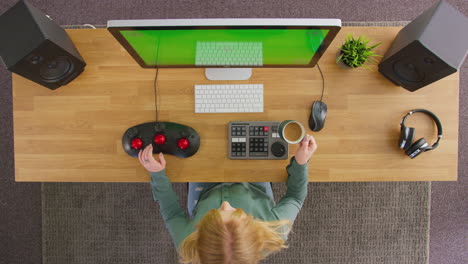 overhead view of female video editor working at computer with green screen in creative office