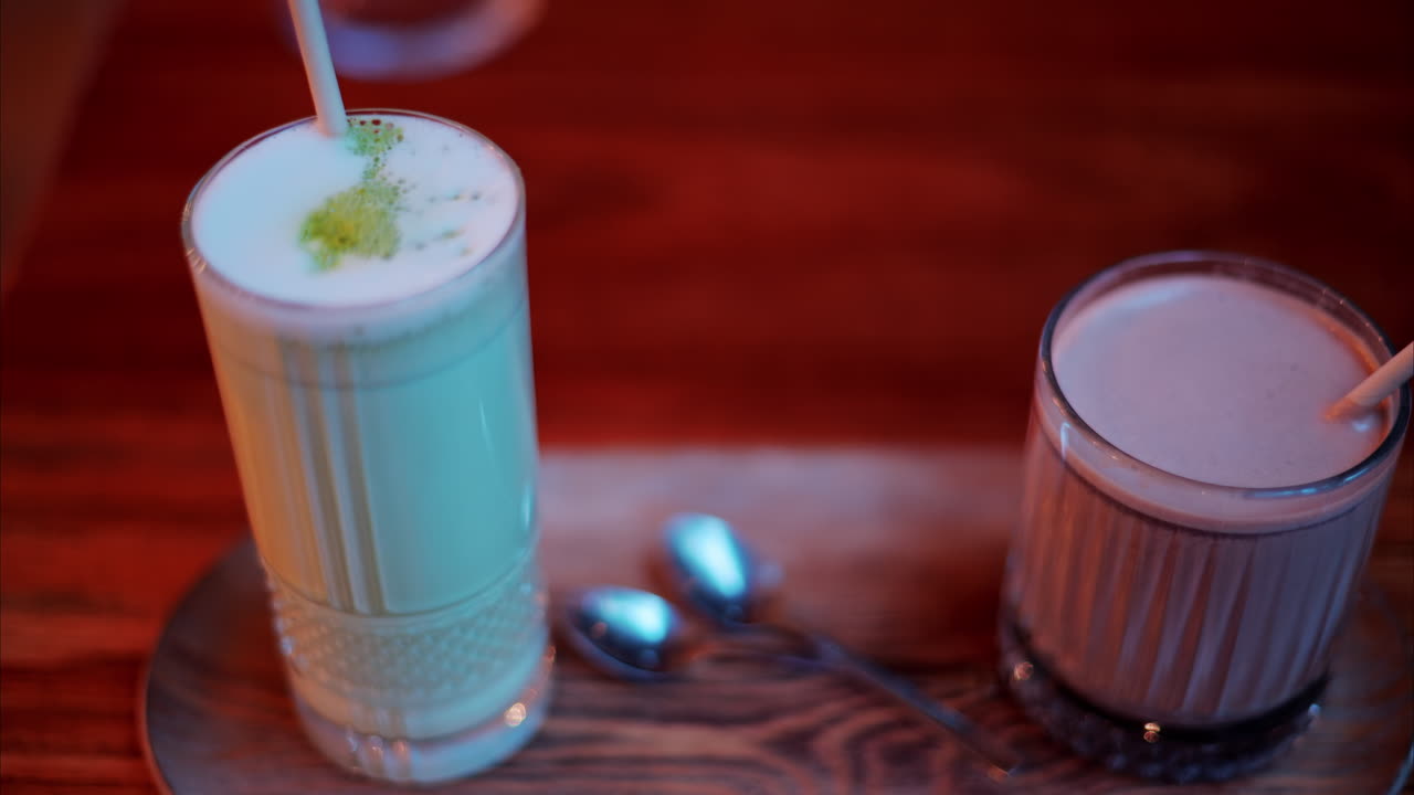 Bir kafede masanın üzerinde, kağıt pipetli bardaklarda sıcak çikolata ve matcha latte yakın çekimi