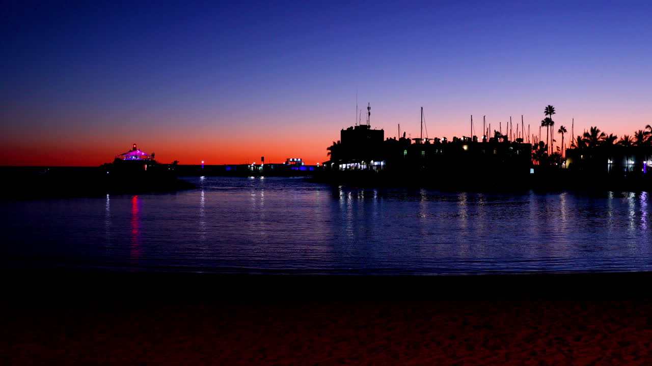 Sunset over the lagoon of orange-red clouds on the horizon and reflections of lights reflecting on sea level with urban area Grand Canary Island Valley 4k slow motion capture at 60fps.