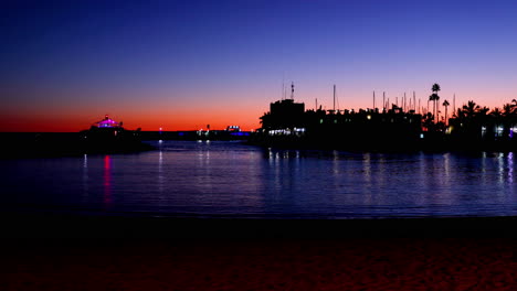 sunset over the lagoon of orange-red clouds on the horizon and reflections of lights reflecting on sea level with urban area grand canary island valley 4k slow motion capture at 60fps.