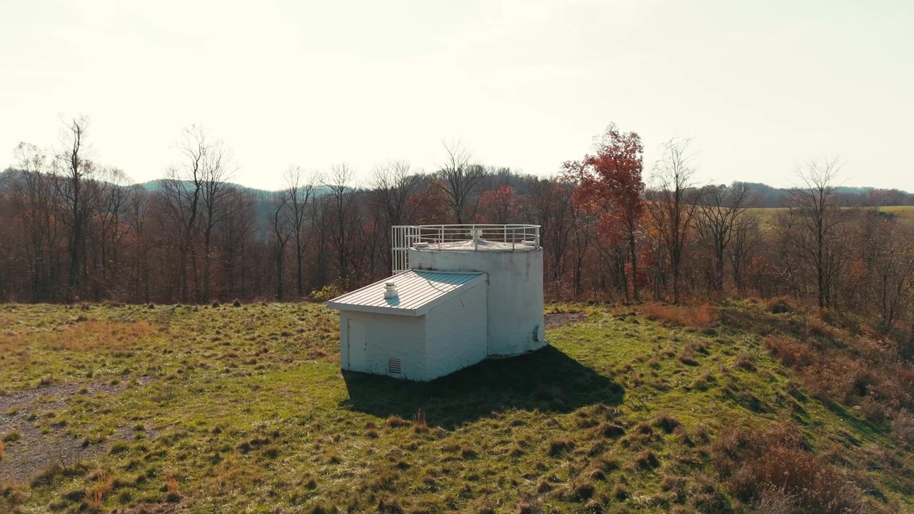 Orbita aerea attorno a un serbatoio d'acqua bianco in un campo aperto, circondato da erba e alberi.