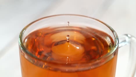 tea droplet making splash crown and ripples in the transparent mug on bright background