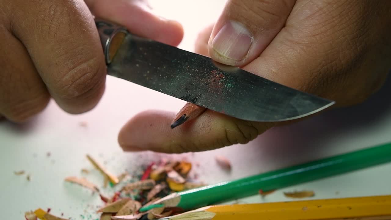 Opptak av hender som sakte spisser en blyant og noen fargeblyanter med en skarp kniv