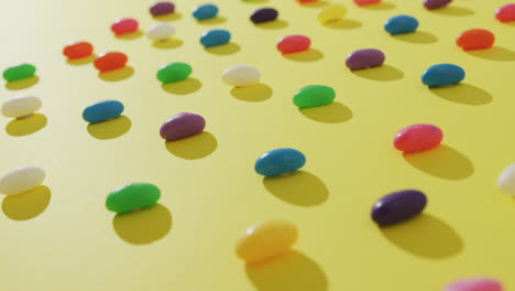 video of overhead view of rows of multi coloured sweets over yellow background