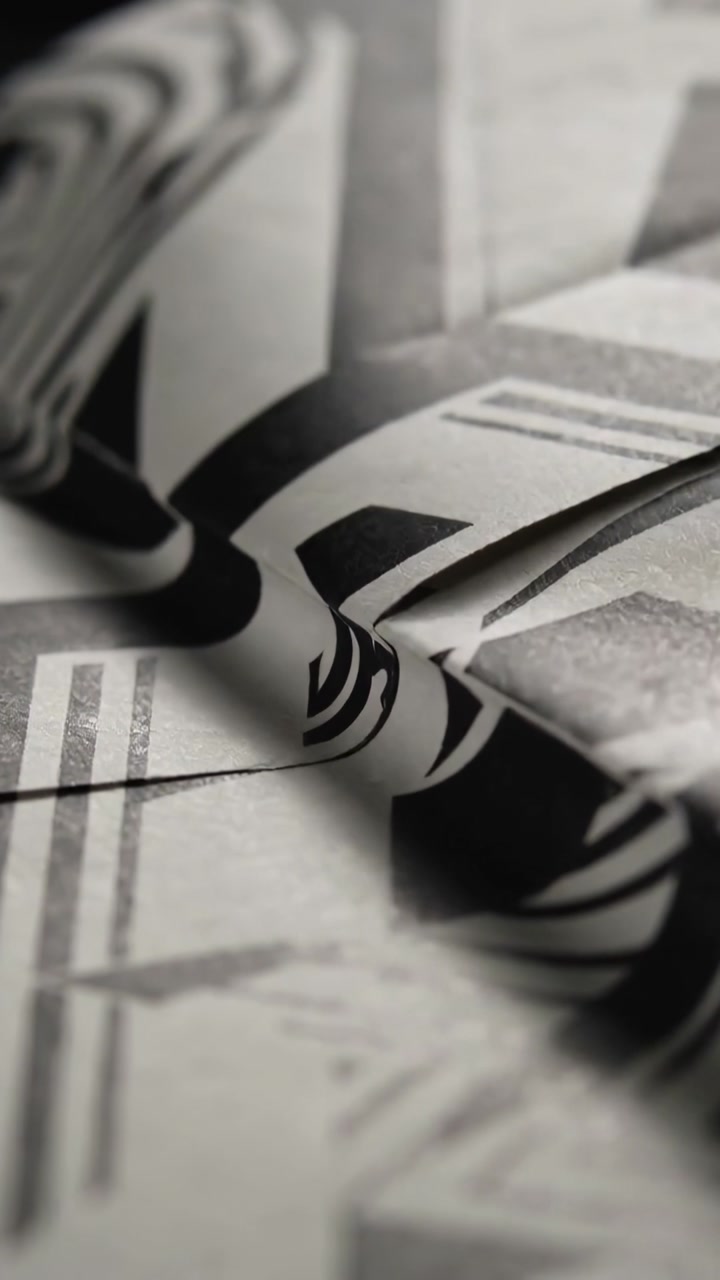 Vertical video: Shifting focus camera showing creased B and W paper on table, exposing fold tip
