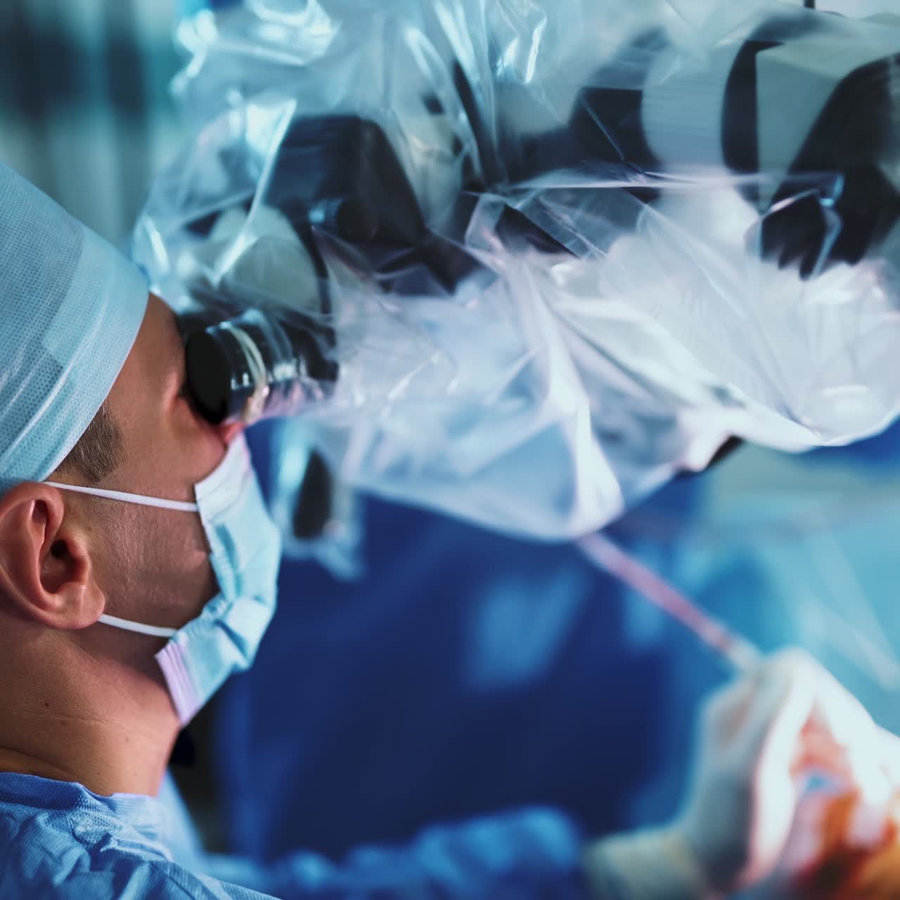 Doctors performing surgery looking at microscope. Two medical professionals wearing special clothes and masks standing their backs to camera. Close up. Blurred backdrop