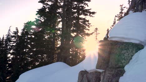 tracking shot revealing sun rays behind snow covered mountain boulder