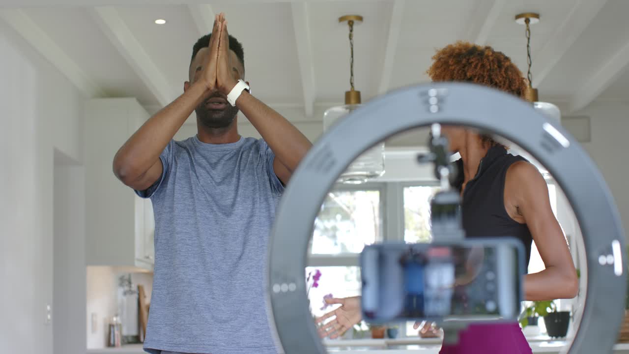 Instructor is cueing and guiding man lowering palms to chest for breathing on phone in kitchen