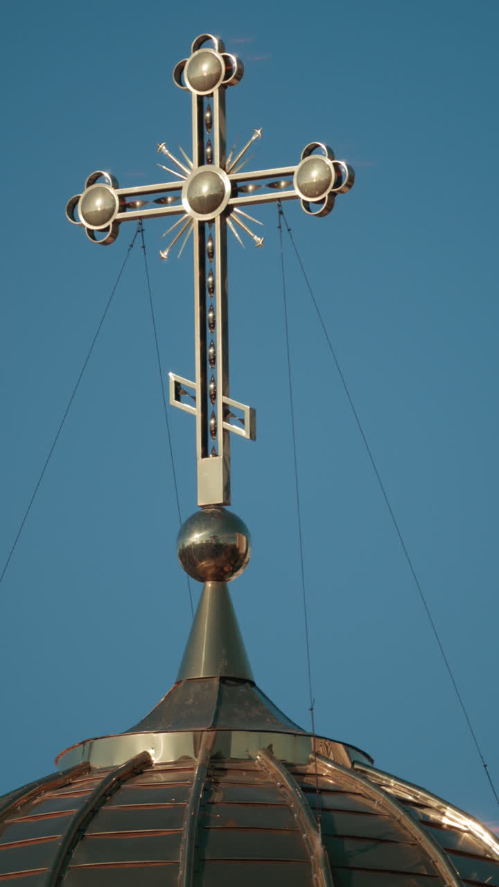 Elegant metallic church cross glowing under clear blue sky. Vertical