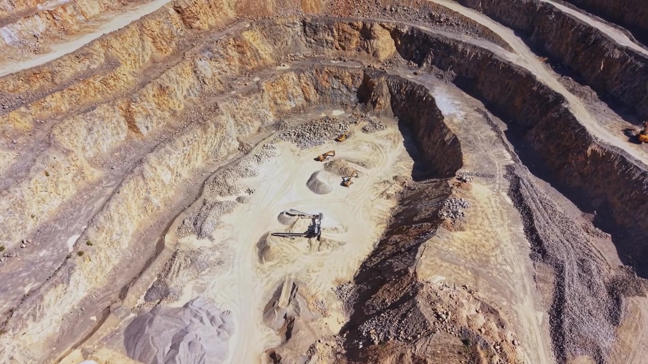 Large quarry site with machinery and mineral piles in clear weather