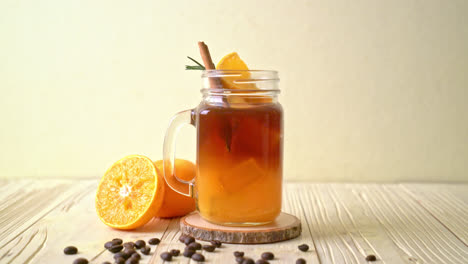 un vaso de café negro americano helado y una capa de jugo de naranja y limón decorado con romero y canela