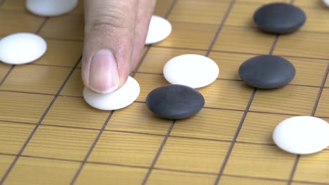 close up on go board or the chinese chess board game, fingers holding a white stone to attack the black stone