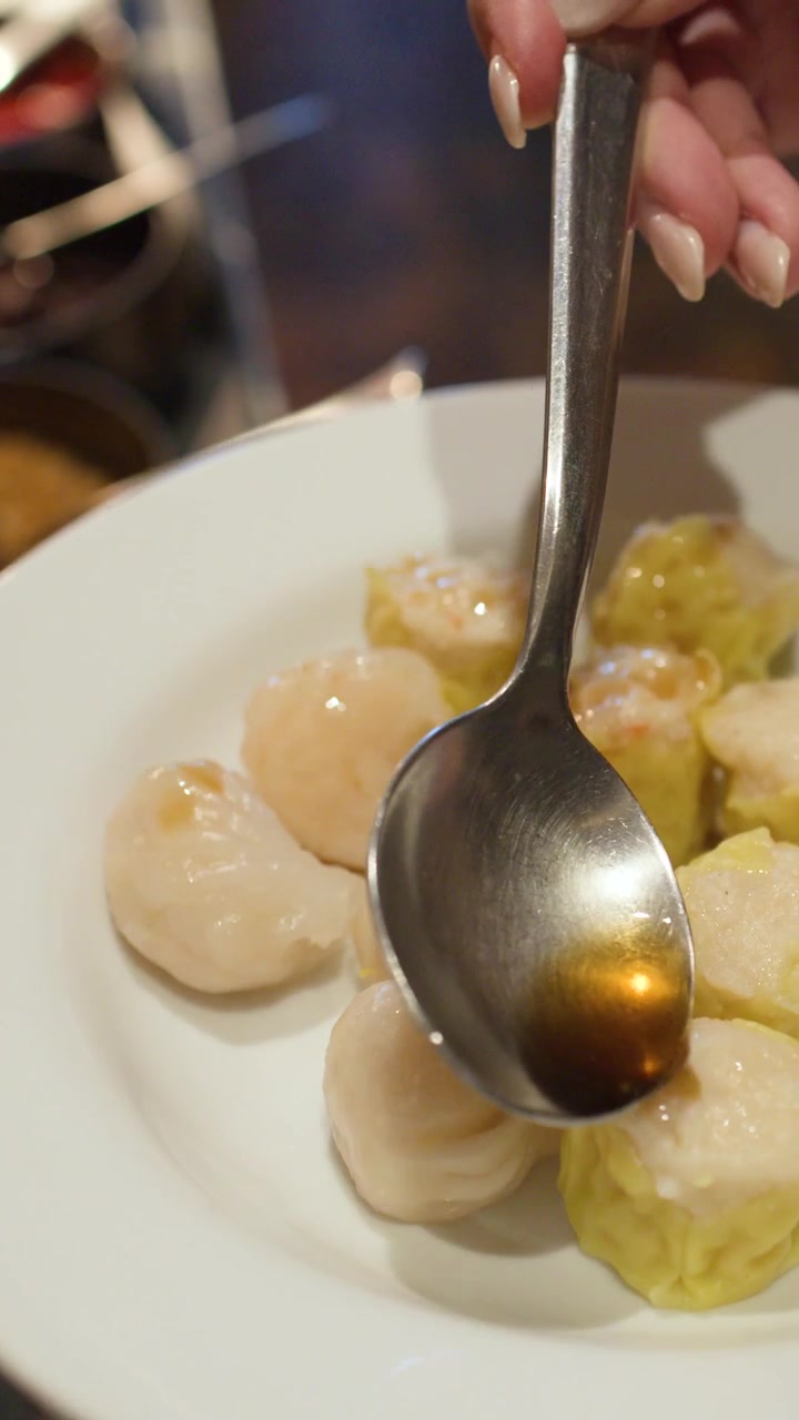 Close-up shot of a hand using a spoon to drizzle sauce over fresh dim sum