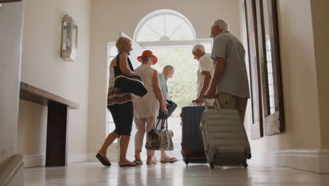 group of senior friends with luggage opening front door and leaving for vacation