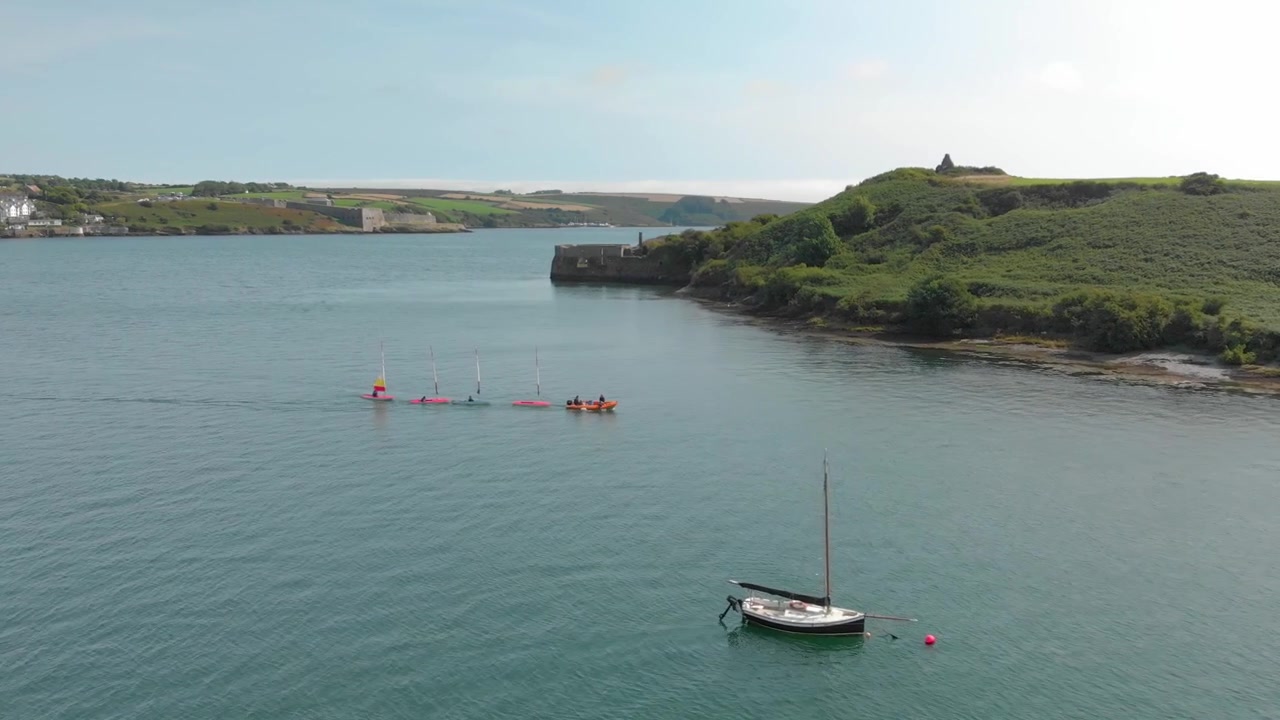 Mentre il vento cala, questi velisti di derive vengono rimorchiati da un motoscafo verso la riva in una splendida serata estiva, a Kinsale Harbour, Contea di Cork, Irlanda