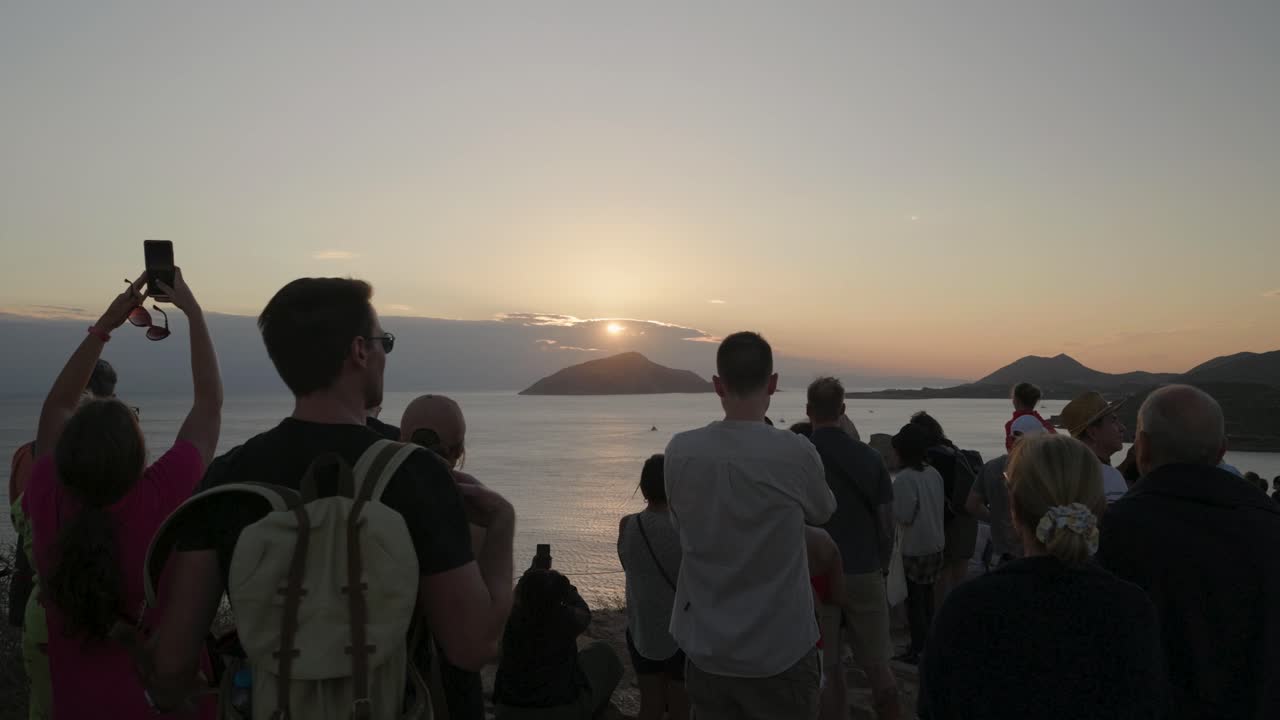 Group of tourists overlooking sunset at cliffs with ocean