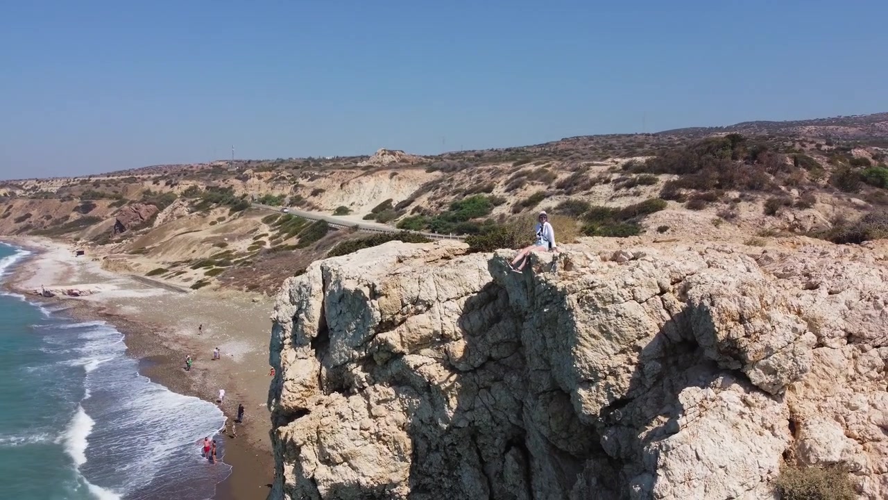 Vista aerea di aspre scogliere costiere che si affacciano su un oceano blu con onde che si infrangono su una spiaggia sabbiosa.