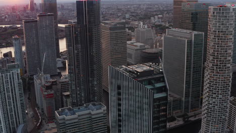 Slide-and-pan-footage-of-futuristic-urban-district.-Tall-office-and-apartments-buildings-in-Canary-Wharf-business-hub-in-sunset-time.-London,-UK