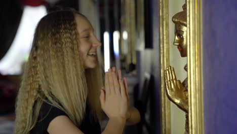 young blonde girl looks at the statue of buddha