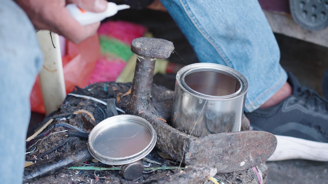Detailed view of a street cobbler workspace in Malaysia with tools, an anvil, glue containers, and worn equipment, highlighting the hands-on repair process and authentic working conditions.