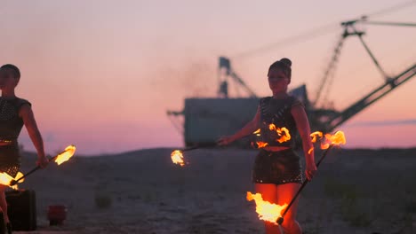 a group of men and woman fire show at night on the sand against the background of fire and tower cranes