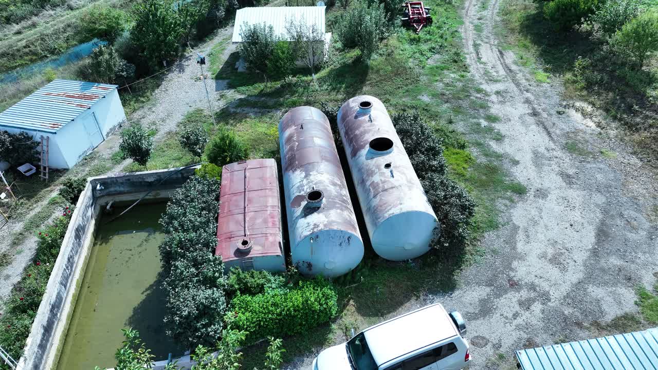 an industrial site with large cylindrical tanks, and a water storage basin. It looks like a rural facility for water treatment or irrigation management, surrounded by trees and open land