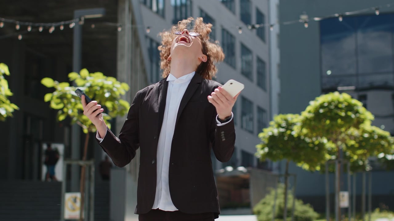 Uomo d'affari arrabbiato, confuso, perplesso, urlando, parlando su due telefoni cellulari sulla strada fuori dall'ufficio.
