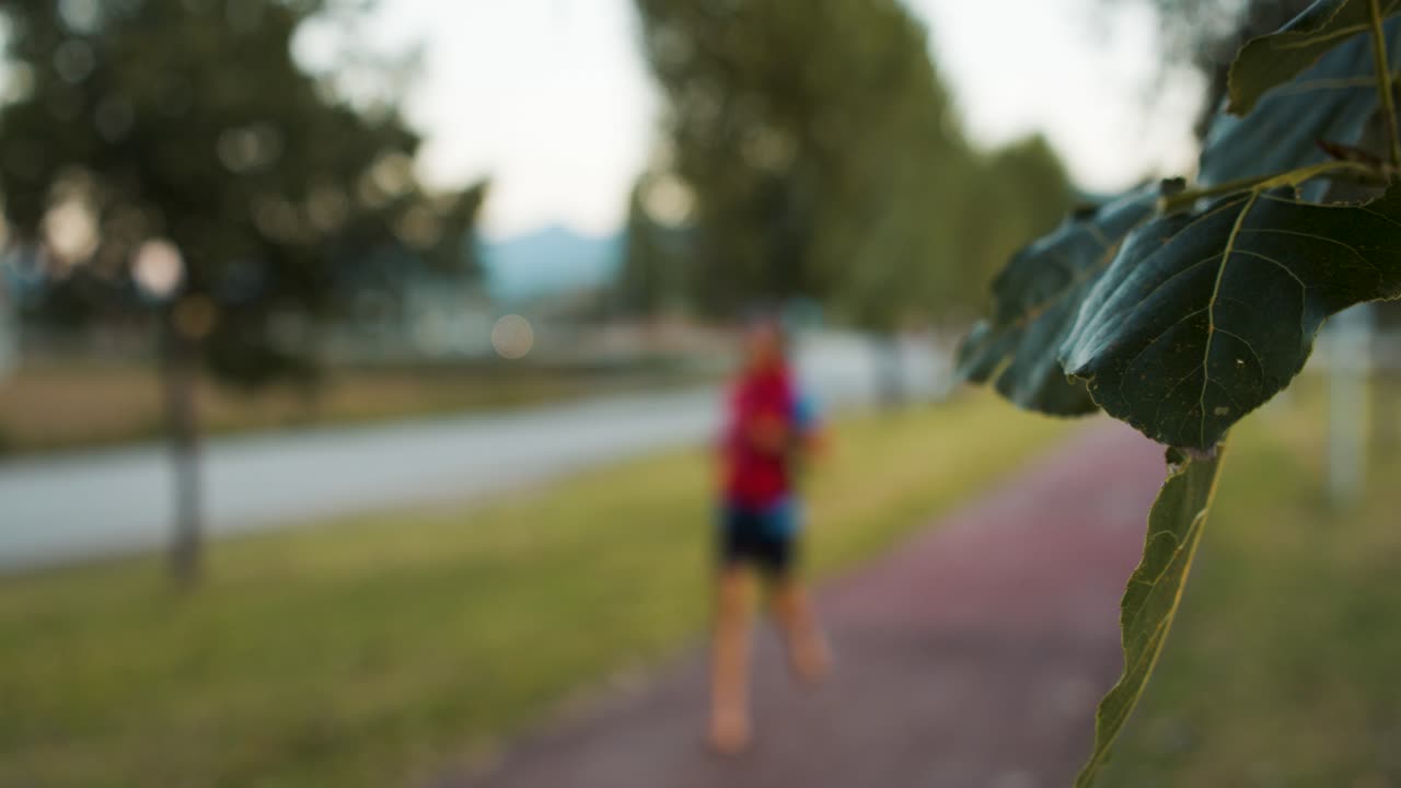 View of a green leaf in the foreground, while a blurry barefoot runner passes by in the background. Nature and sport