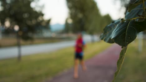 view of a green leaf in the foreground, while a blurry barefoot runner passes by in the background. nature and sport