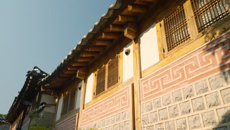 low angle view of intricate wooden eaves, tiled roof, and patterned stone wall of a hanok in bukchon hanok village, jongno-gu, seoul - revealing out of tree branches